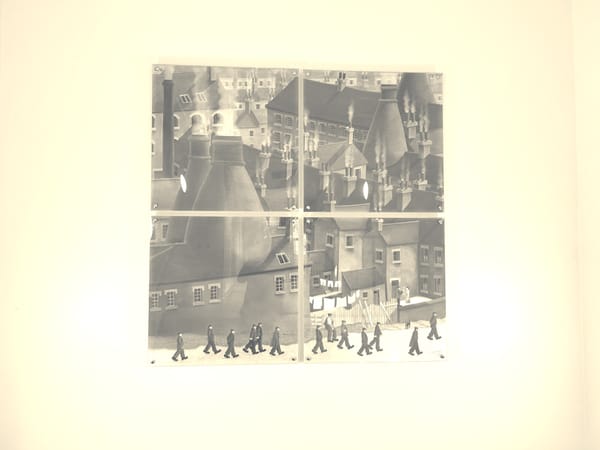 A picture of Victorian factory workers going to work in the potteries. There are distinct bottle kilns (shaped like bottles, local to the area) coming out of the roofs of the buildings. 